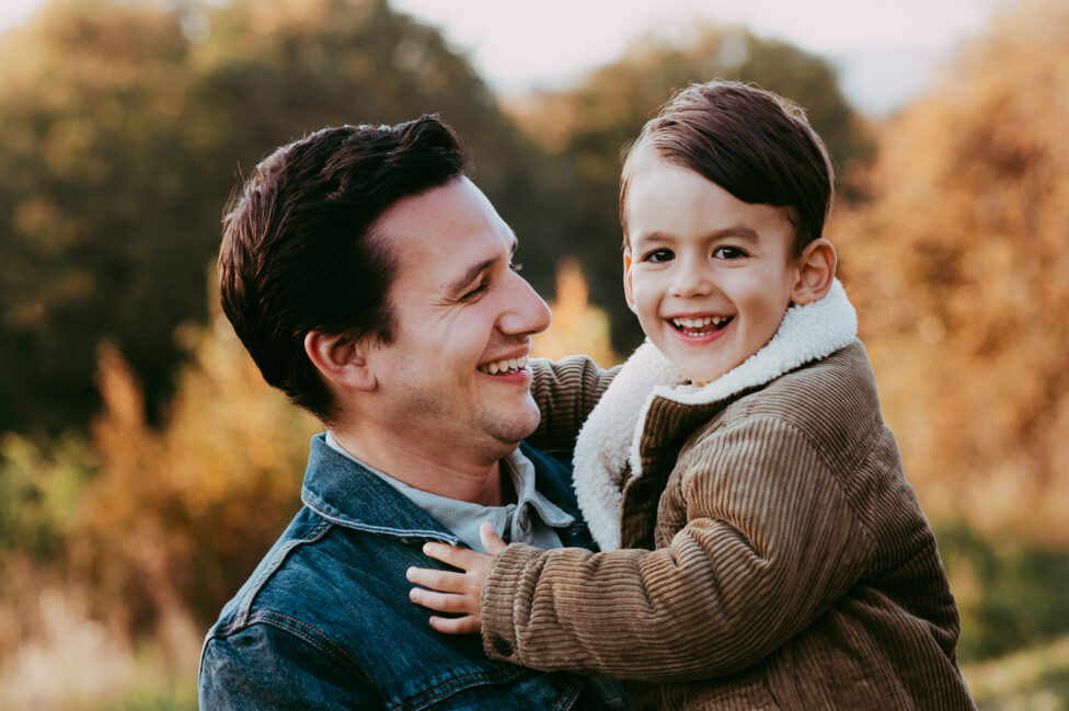 Kleiner Junge lacht strahlend und Papa hält ihn auf dem Arm.