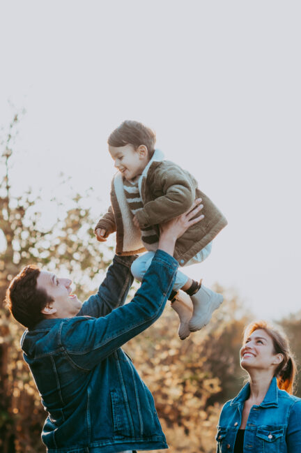 Eltern schauen auf Sohn, den der Papa in die Luft stemmt.