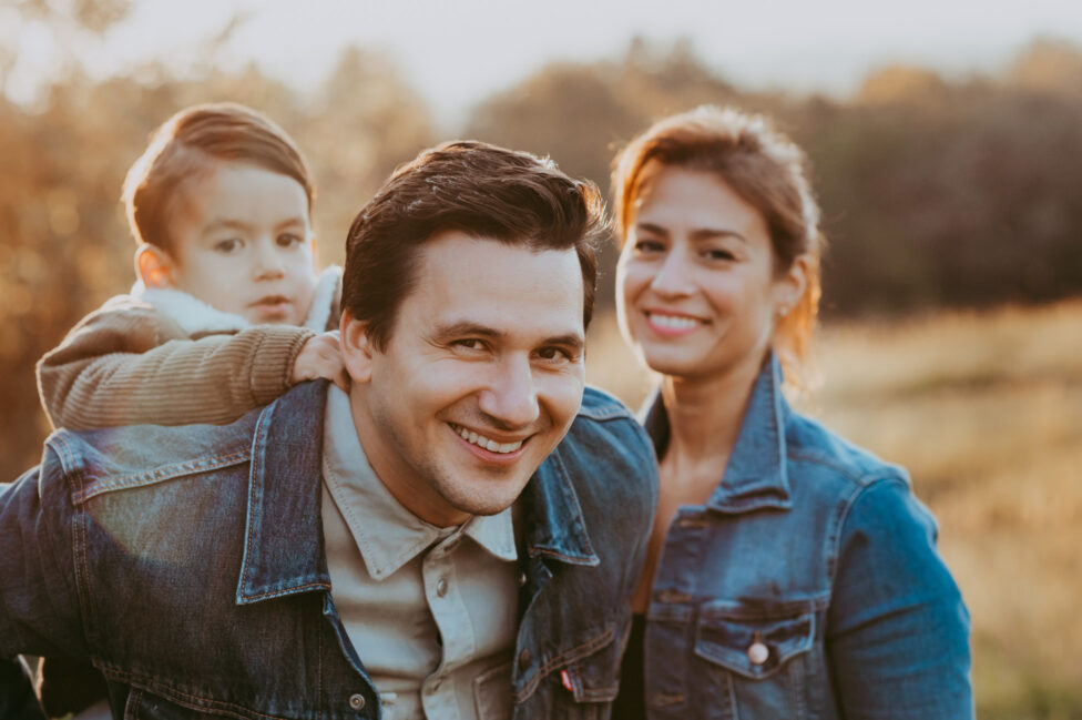 Papa trägt den Sohn auf dem Rücken und Mama lacht im Hintergrund