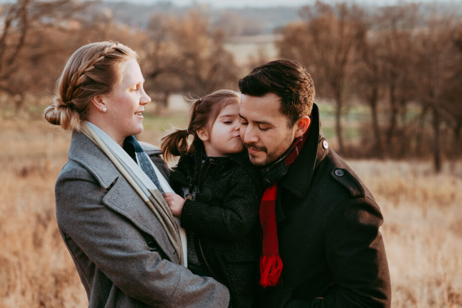 Eltern und Tochter auf einer herbstlichen Wiese, Tochte rgibt Papa einen Kuss