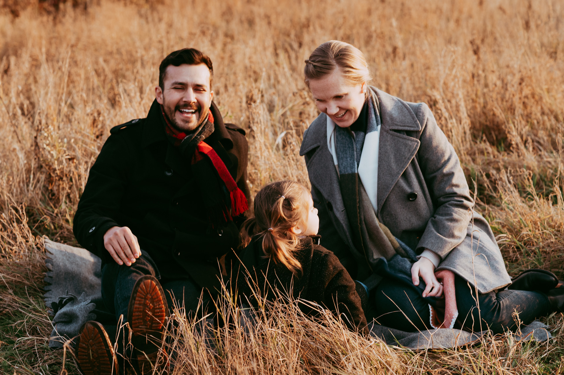 Eltern und Tochter auf einer herbstlichen Wiese, Kind schaut weg und Eltern lachen